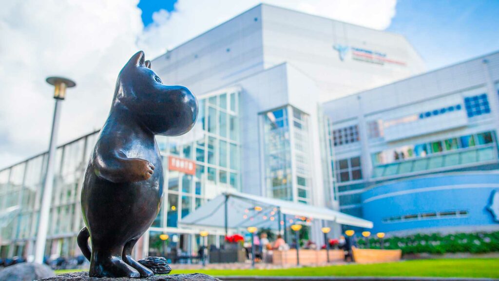 A bronze statue of the Moomin troll is outside of a large building.