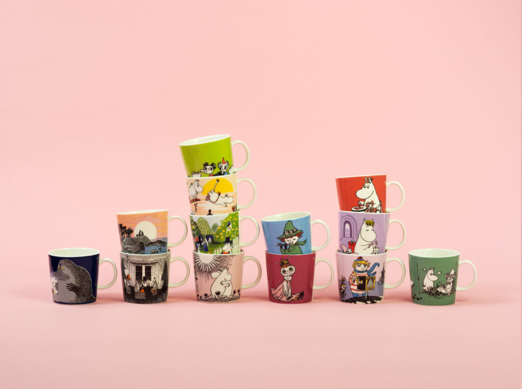 Different Moomin mugs on a pink background.